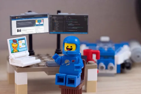 A lego spaceman sitting at a desk with computer monitors